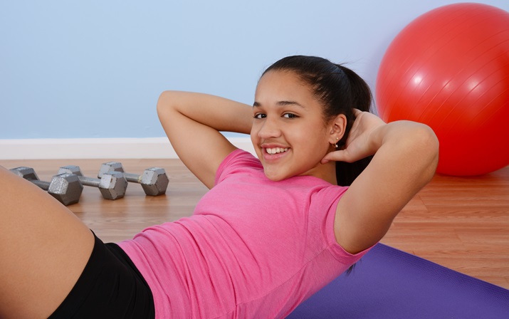 Happy teenage girl doing sit-ups with other fitness equipment in the background