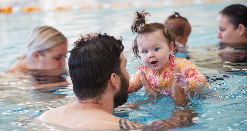 Father with baby daughter participating in parent baby swim class